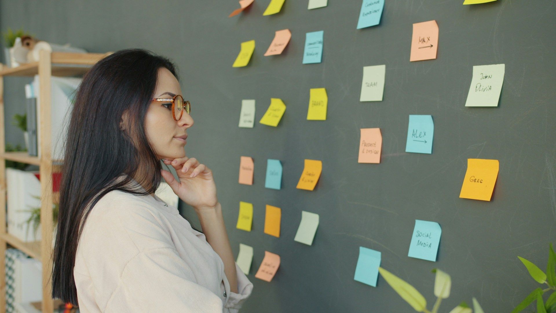 Woman studying a wall of colorful sticky notes, thinking