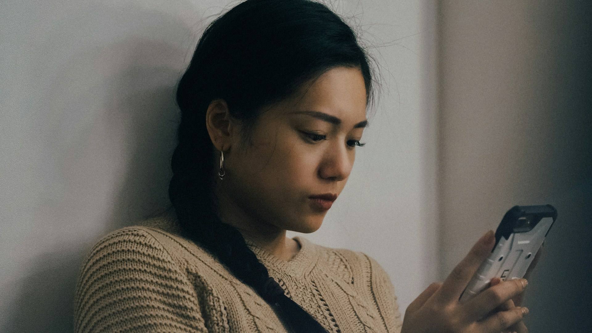 Woman leaning against a wall checking her phone, the pull to answer right away